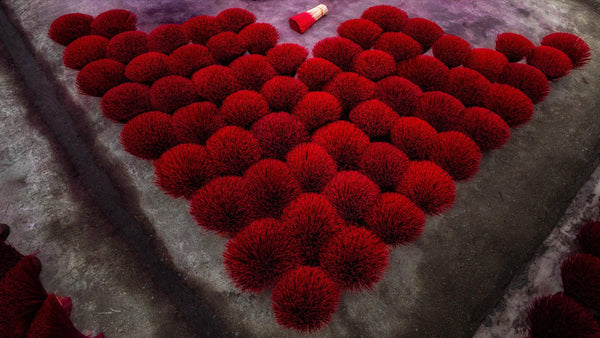 Heart-shaped arrangement of vermilion incense bundles on concrete, with a single bundle placed above as a focal point.