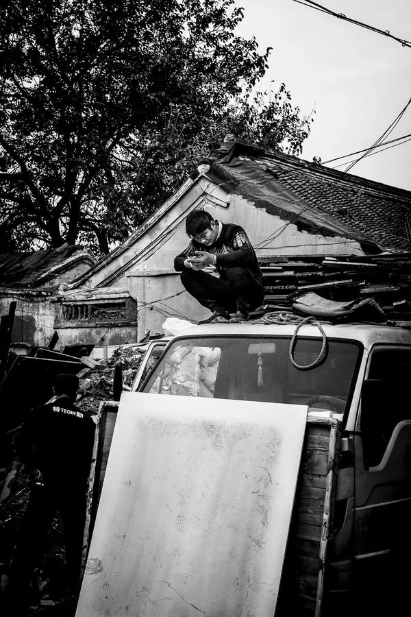 Street Scene of a local worker enjoying break time while sitting on his car's roof in the hutong around Yong He Gong Da Jie, Beijing, China.  Fine Art Limited Edition of 28. Photo © Copyright by Sylvère Clerempuy.