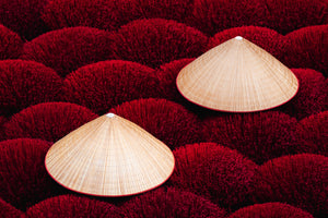 Top-down composition of two Vietnamese conical hats placed on dense red incense bundles in an incense-drying yard.