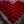 Heart-shaped arrangement of vermilion incense bundles on concrete, with a single bundle placed above as a focal point.