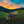 Two water buffaloes grazing in a field with a colorful sunset sky and mountains in the background.